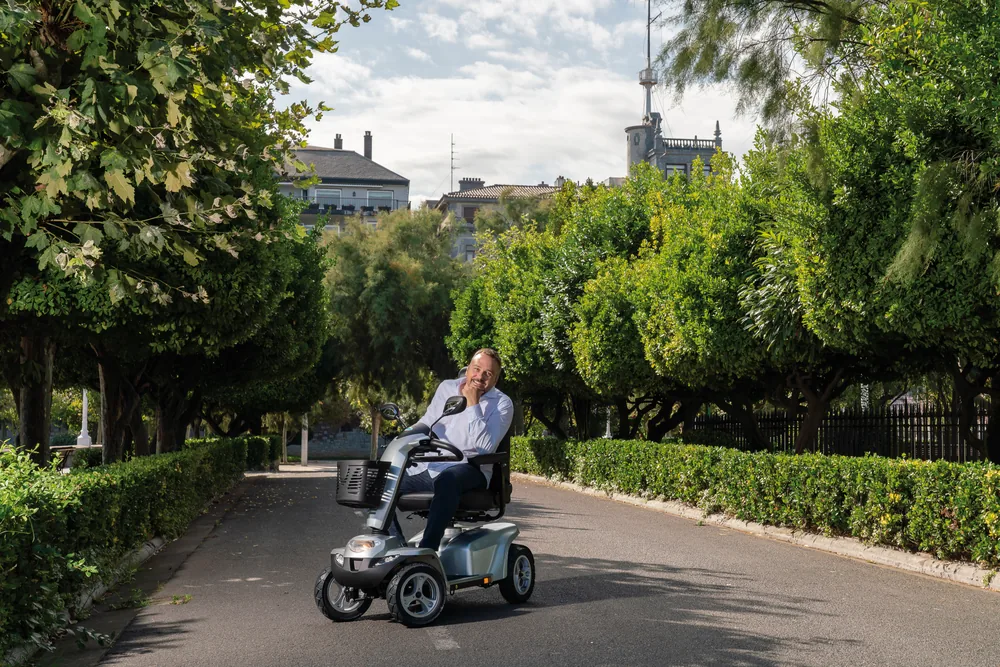 Hombre conduciendo el scooter eléctrico I-Galaxy de Wellell por un paseo arbolado