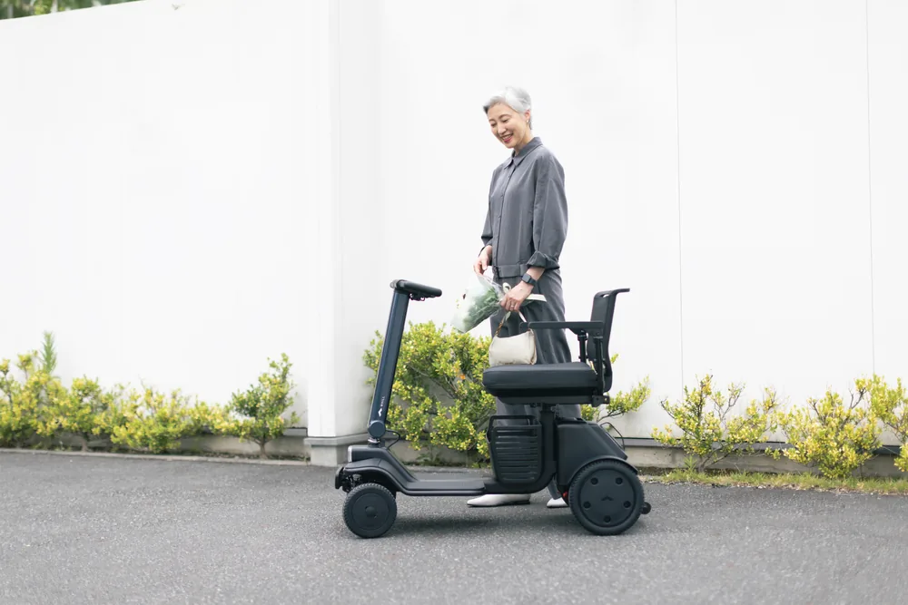 Mujer de pie junto al scooter eléctrico WHILL Model R