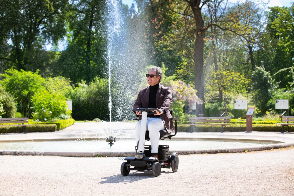 Hombre conduciendo el scooter WHILL Model R en un parque con una fuente