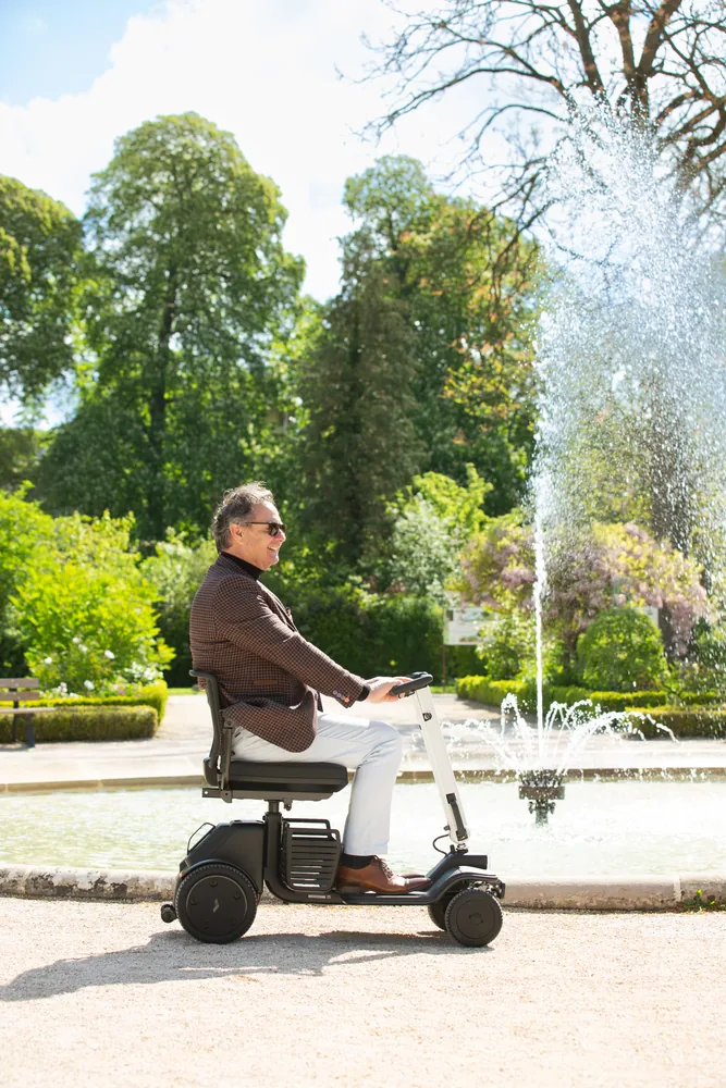 Hombre en el scooter eléctrico WHILL Model R junto a una fuente