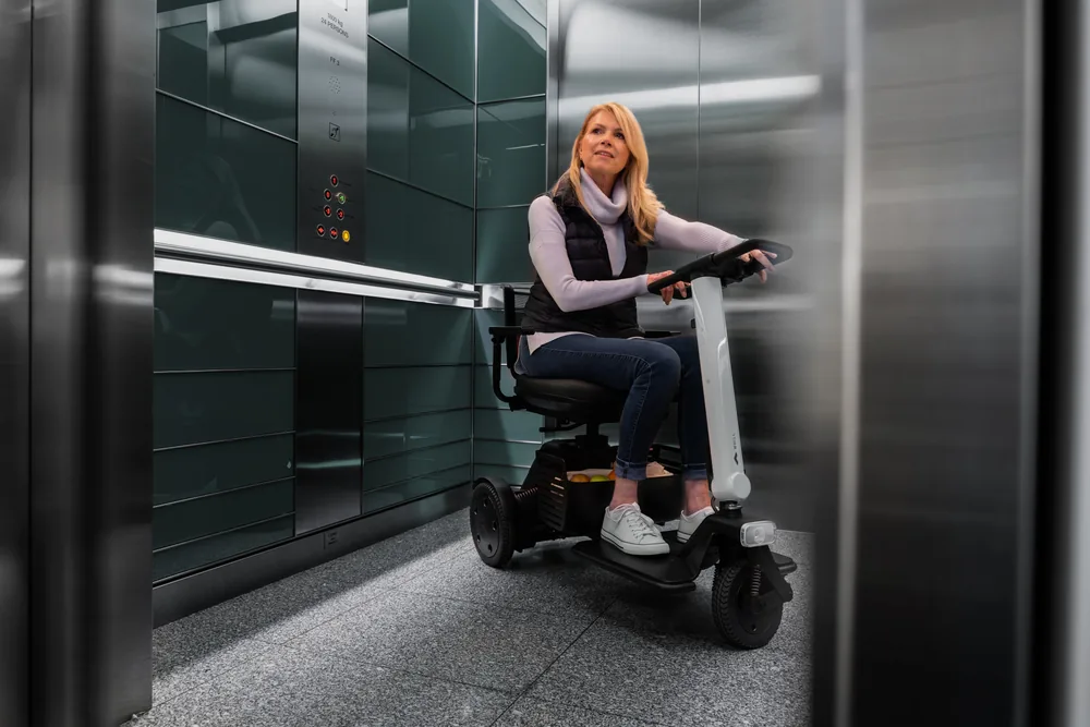 Mujer con el scooter WHILL Model R de 3 ruedas dentro de un ascensor