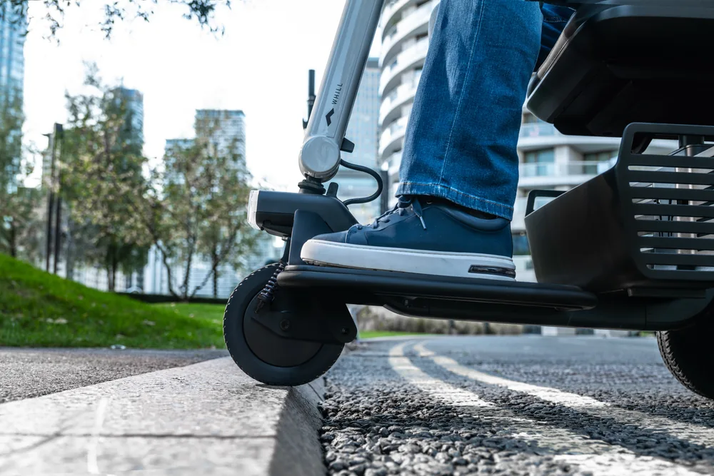Scooter WHILL Model R de 3 ruedas superando un bordillo