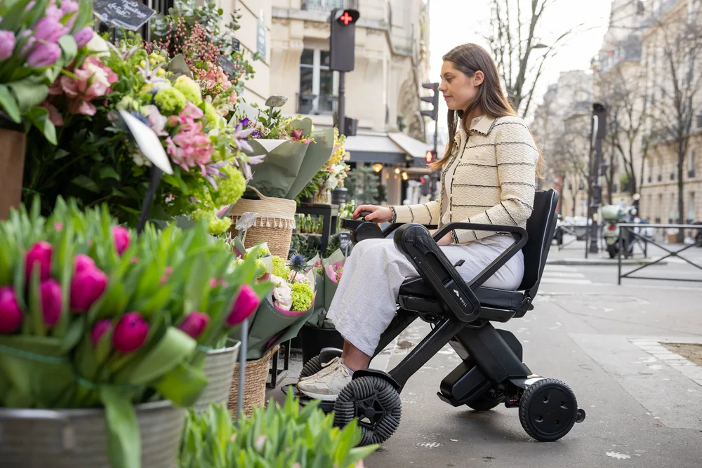 Mujer en la silla WHILL Model C Lite frente a una floristería
