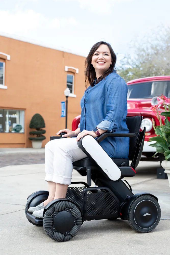 Mujer sonriente en la silla de ruedas eléctrica WHILL Model C2 en la calle
